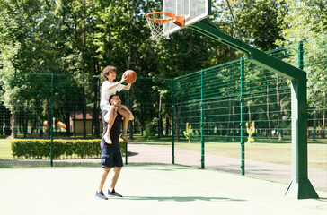 Wall Mural - Happy father helping his son to score a basket