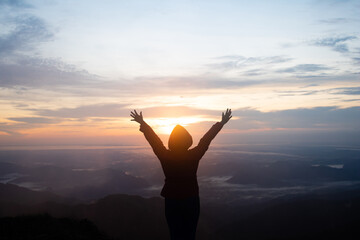 Silhouette women standing on cliff and see sun up.She is raise hand up and enjoying fresh air.She enjoying free happiness in beautiful Thailand landscape. photo concept active and nature background.