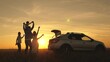 parents and children stopped for break by car. dad with daughter on his shoulders, mom and children dance and admire beautiful sunset. happy family travels by car. Car travel concept. healthy family