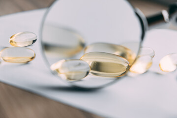 yellow transparent omega 3 capsules under a magnifying glass. vitamin development concept