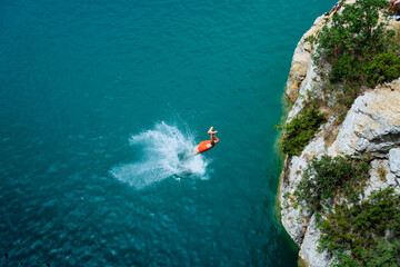 Junger Mann spring von einer Klippe  ins blaue Meer