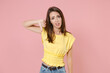 © ViDi Studio - Displeased dissatisfied young brunette woman 20s wearing yellow casual t-shirt posing standing showing thumb down looking camera isolated on pastel pink color wall background studio portrait.