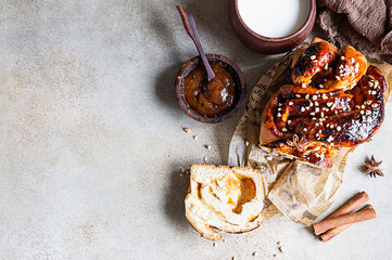 Poster - Apricot jam twisted loaf bread or babka with nuts and spices on concrete background with a cup of milk. Homemade yeast bun babka. Top view, copy space.