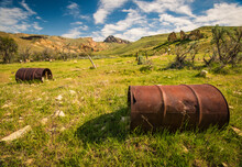 View Of Rusty Barrels On Grassy Landscape Against Cloudy Sky