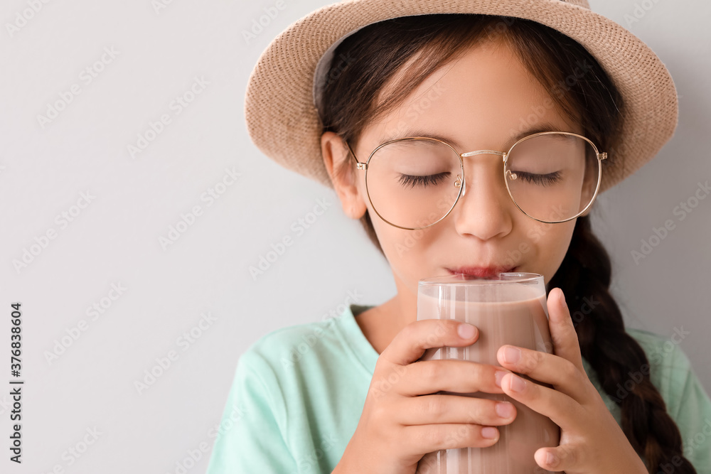 Little girl drinking tasty chocolate milk on light background