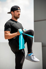 Wall Mural - Handsome Hispanic man warming up with elastic resistance band before exercise outdoors at rooftop - home open air work out concept