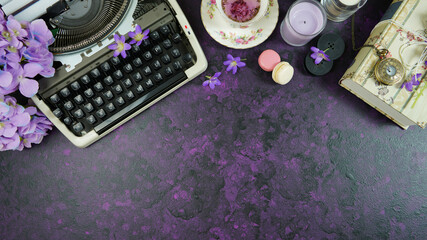Wall Mural - Purple theme vintage writers desktop workspace with typewriter, lavendar tea, hibiscus flowers and old books on stylish purple textured background. Top view blog hero header creative flat lay.