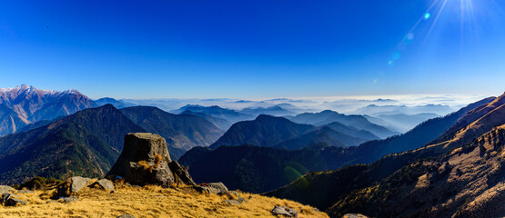 Wall Mural - View of Himalayas mountain range with visible silhouettes through the colorful fog from Khalia top trek trail. Khalia top is at an altitude of 3500m himalayan region of Kumaon, Uttarakhand, India.