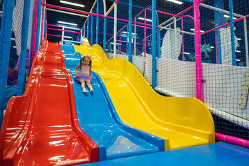 Happy little baby, 4 year old girl, children ride up, down slide in play center