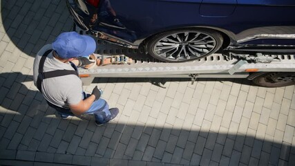 Wall Mural - Newly Purchased Vehicle At Car Dealership Being Unloaded From Flatbed Truck. Driver Unhooking And Folding Safety Straps. 