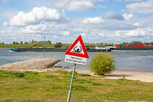 Odd Road Sign Along The Waal River In Zaltbommel, Gelderland: Dangerous Swimming (in Dutch) And Risk Of Drowning; A Cargo Ship Passes By 
