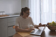 © stokkete - Woman sitting at the kitchen table and connecting with her laptop