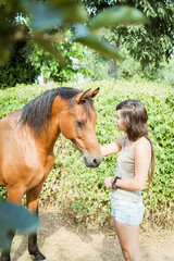 Girl with dreadlocks stroking her brown horse.