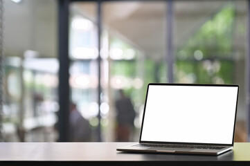 Mock up empty screen laptop on wooden table with space for product display, blurred modern office background.