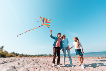 Wall Mural - Family with child and kite holding hands on beach near sea