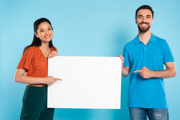 Wall Mural - asian woman in red blouse and man in polo t-shirt pointing with fingers at blank placard on blue