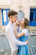 © Sofiia Shunkina - Romantic shot of funny lovely young couple, walking outdoors in the city, posing to camera with tasty macarons, feeding each other, on the background of vintage building with blue door