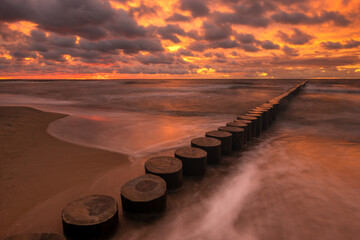 Wall Mural - minimalist landscape showing sea waves and a breakwater at sunset