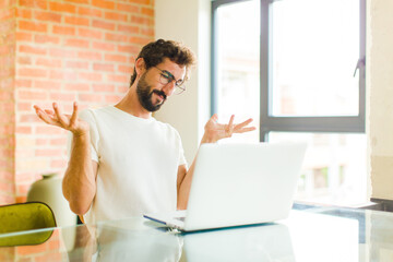 Wall Mural - young bearded man with a laptop looking puzzled, confused and stressed, wondering between different options, feeling uncertain