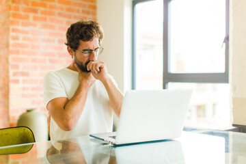 young bearded man with a laptop feeling ill with a sore throat and flu symptoms, coughing with mouth covered