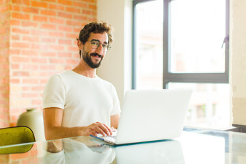 Wall Mural - young bearded man with a laptop smiling positively and confidently, looking satisfied, friendly and happy