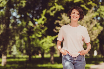 Wall Mural - Photo of charming cute lady hands pockets toothy shiny beaming smiling walking park relaxing green trees nature healthy atmosphere chilling wear white shirt denim jeans outdoors