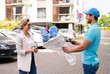 © blackday - Young delivery man in blue uniform delivers flowers to a woman client
