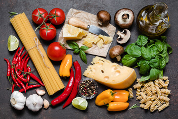 Wall Mural - Italian food cooking ingredients on dark background - pasta, basil, tomato, cheese, olive oil, mushrooms, spices.