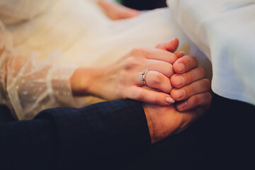 The groom holds the bride's hand at the wedding ceremony. Hold hands and walk together. Confidence. On the bride s hand is a white gold ring with black diamonds.