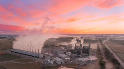 Wall Mural - Power plant under colorful twilight sky, steaming amid foggy rural landscape.
