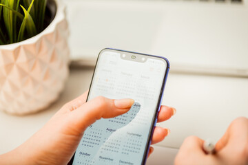 Woman holding phone and using calendar to make her plan in the notepad