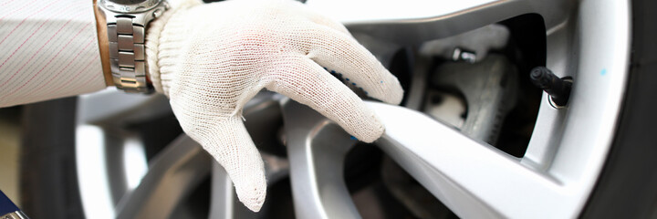 Wall Mural - Close-up of persons hand wearing work gloves and working with car wheel. Clipboard with checklist information. Garage and repair service station concept