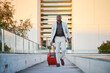 © Cavan Images - African-American man in a stylish suit and a red suitcase walking down a wooden walkway at sunset