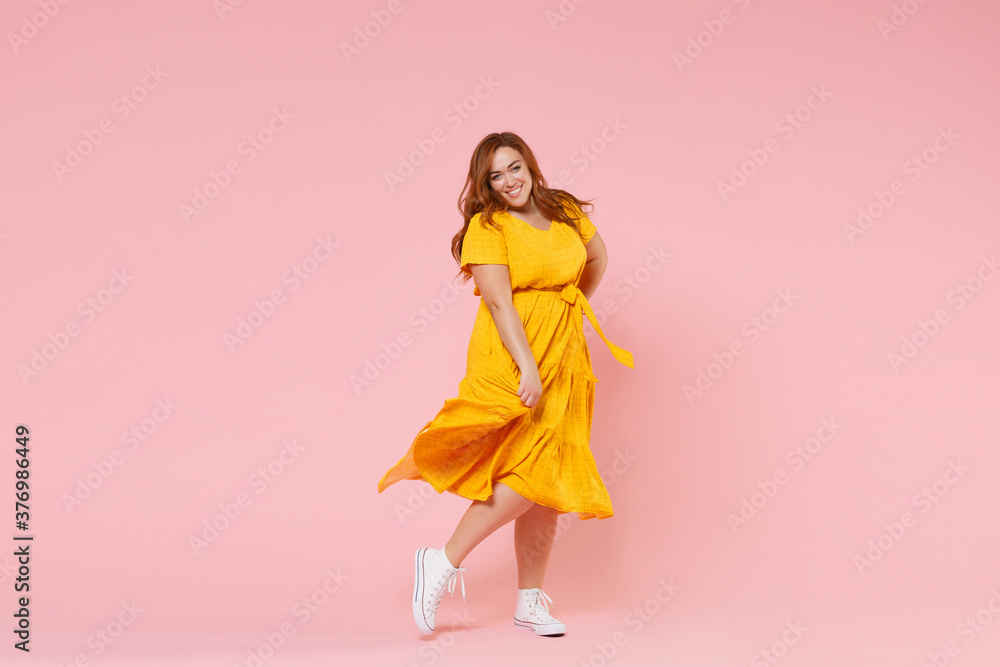 Full length portrait of smiling beautiful charming young redhead plus size body positive female woman girl 20s in yellow dress posing looking camera isolated on pastel pink color background studio. - obrazy, fototapety, plakaty 