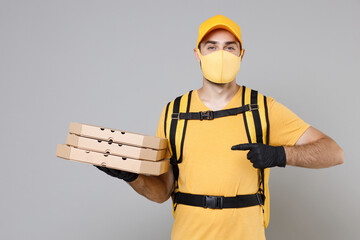 Wall Mural - Delivery employee man in yellow cap face mask gloves t-shirt thermal bag backpack with food hold pizza in cardboard flatbox work courier service quarantine covid-19 virus isolated on gray background.