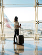 © Cavan Images - Young woman standing with baggage near the airport window waiting for the flight