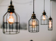 © Cavan Images - lightbulbs protected by wire hang in front of a white wall inside