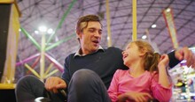 Authentic Shot Of A Happy Smiling Family Is Having Fun To Drive And Crush Bumper Cars At Fun Fair In Amusement Park With Luna Park Lights At Night.