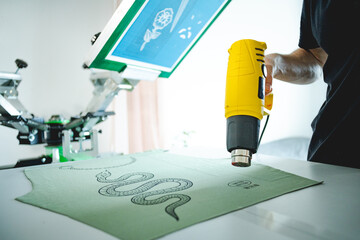 Wall Mural - Man holding heat gun while drying cloth after screen printing press in workshop 