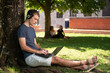 © Egoitz - A blond young male student working on his laptop sitting under a tree in the park.