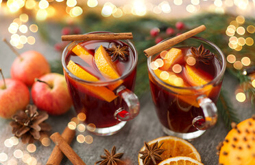 christmas and seasonal treats concept - glass of hot mulled wine with orange slice, apples and fir branch on grey background