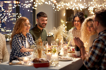 Wall Mural - holidays and celebration concept - happy friends having christmas dinner at home with bottle of non-alcoholic red wine