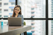 © Nopphon - Young asian businesswoman using laptop sitting in modern office working with social distancing alcohol gel on desk.