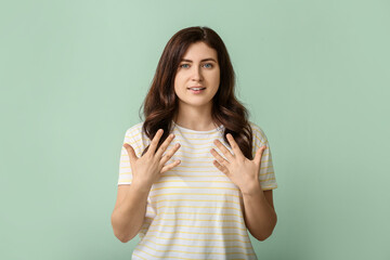 Young deaf mute woman using sign language on color background