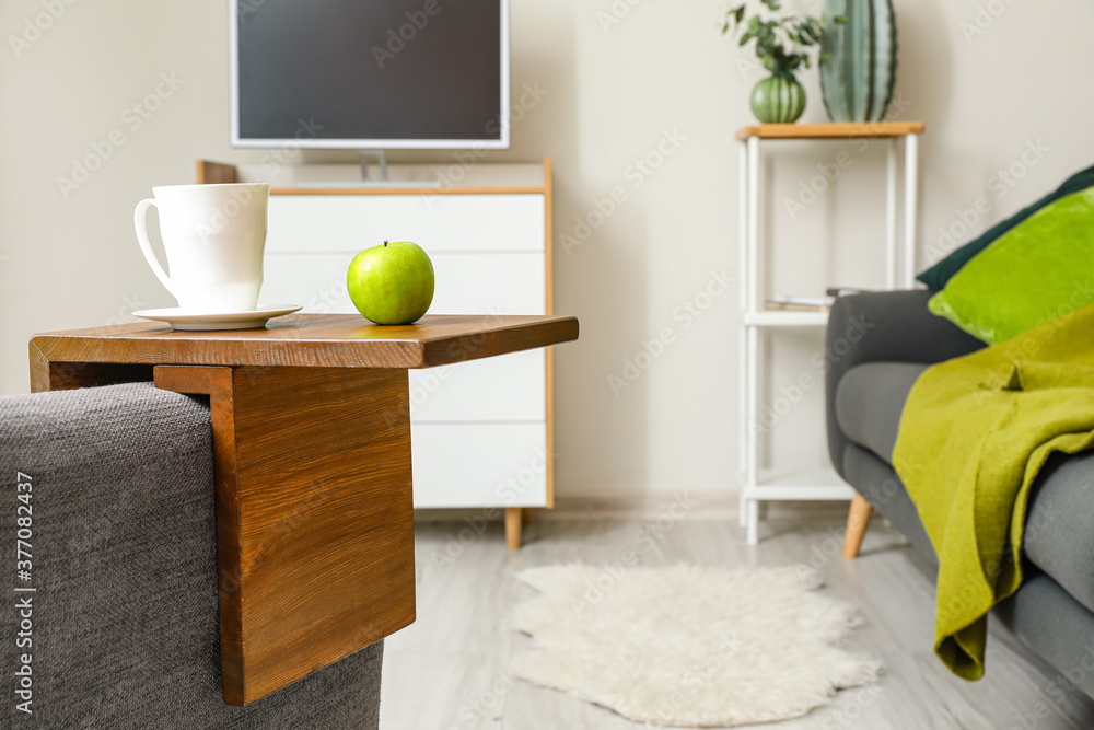 Cup of tea with apple on armrest table in room