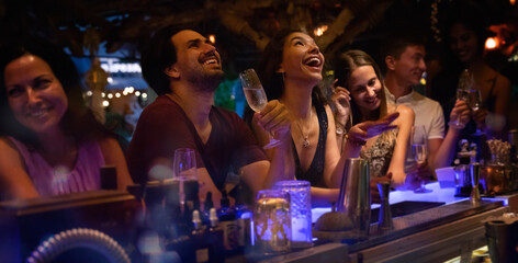 Wall Mural - Group of young people having fun at a party at the bar, laughing and drinking alcohol