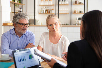 Financial insurance agent meeting with young and mature customers at co-working, showing agreement and explaining details. Businesswoman using laptop with graphs on display. Business meeting concept