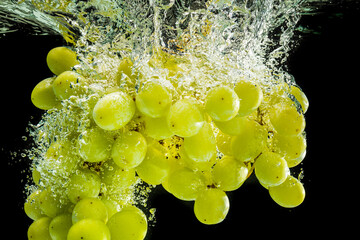 Wall Mural - Bunch of white grapes splashing into clear water isolated against black background. Food splash photography