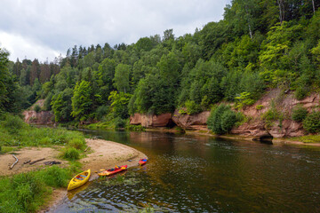 landscape with sandstone cliffs, canoes and kayaks on the river bank, fast flowing and clear river water, Kuku cliffs, Gauja river, Latvia