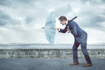 Businessman with an umbrella is facing strong headwind